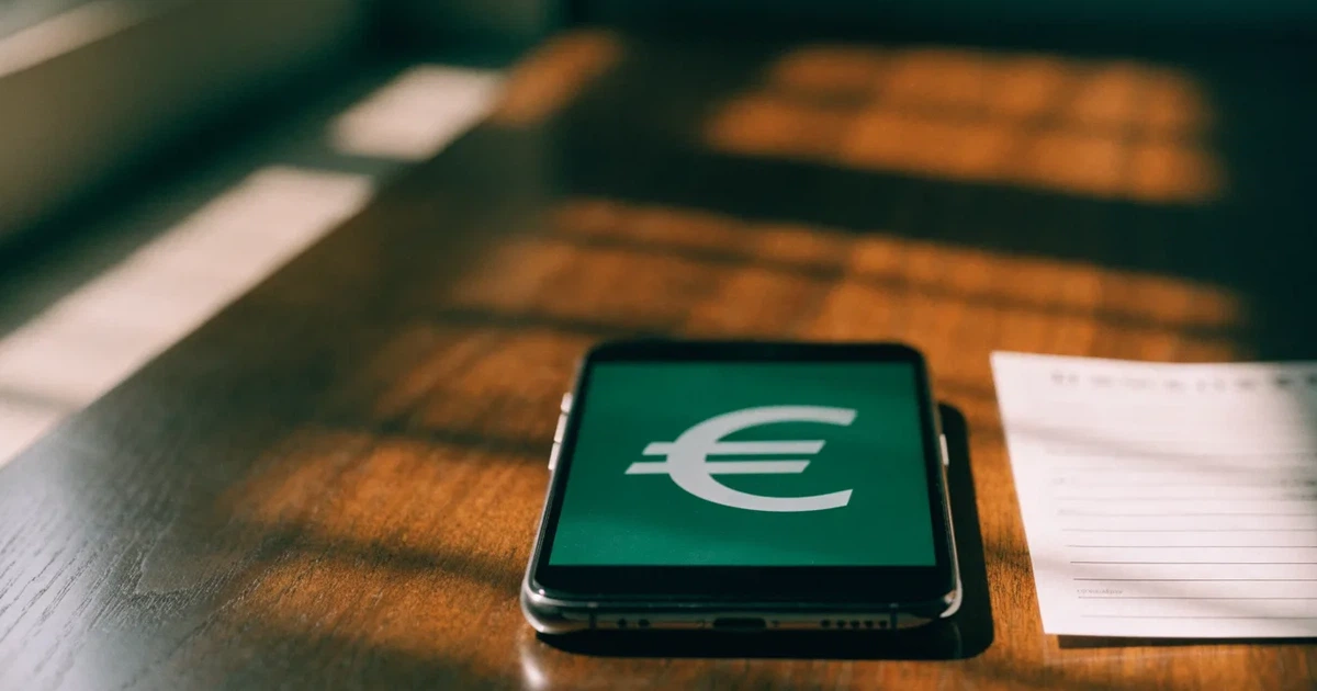 Uma moeda física de bitcoin ao lado de um telemóvel com um talão de aposta no ecrã, sobre uma mesa escura