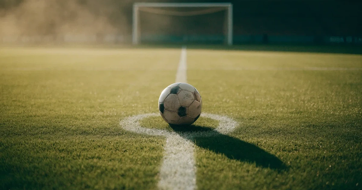 Uma bola de futebol no ponto central de um relvado, à luz da manhã